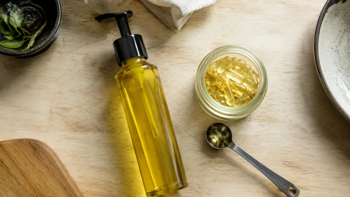 A pump bottle of oil next to a jar of oil capsules on a wood kitchen counter.
